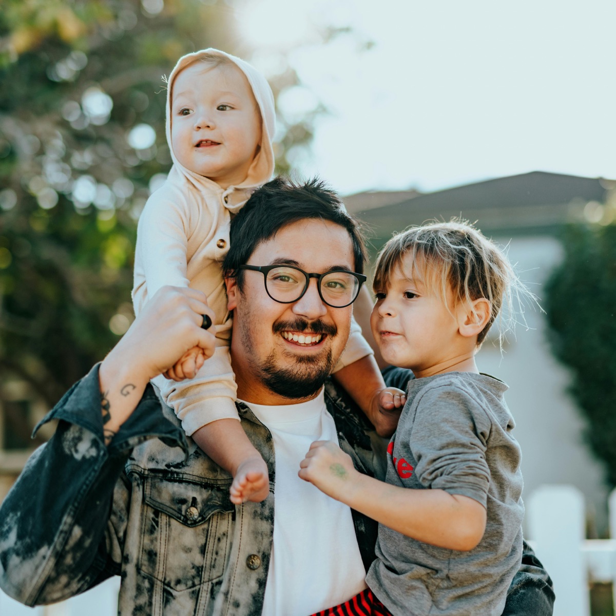 A parent carrying two young children outdoors
